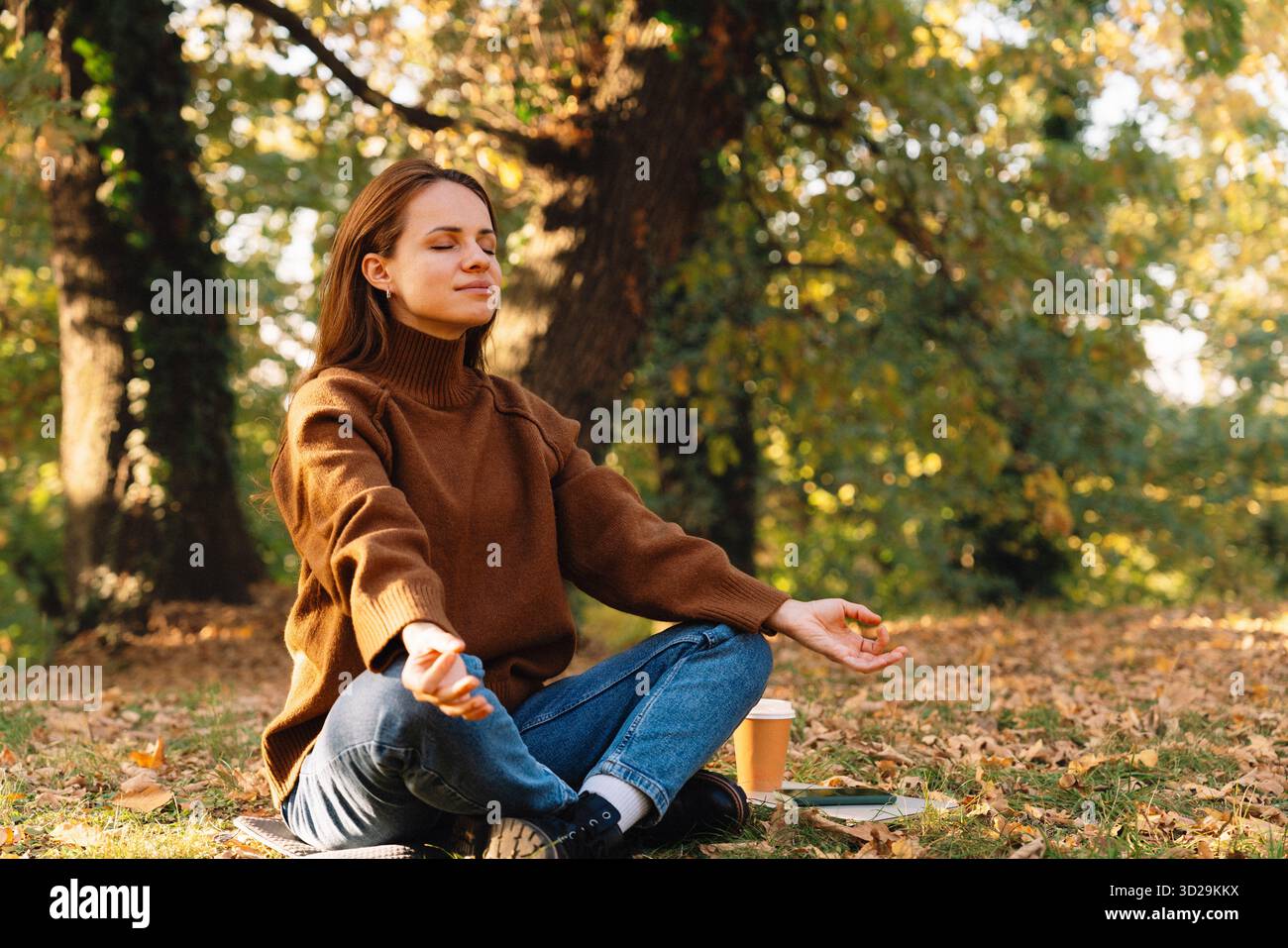 Donna seduta all'aperto per terra con gambe incrociate e meditazione. Terapia forestale e recupero. Foto Stock