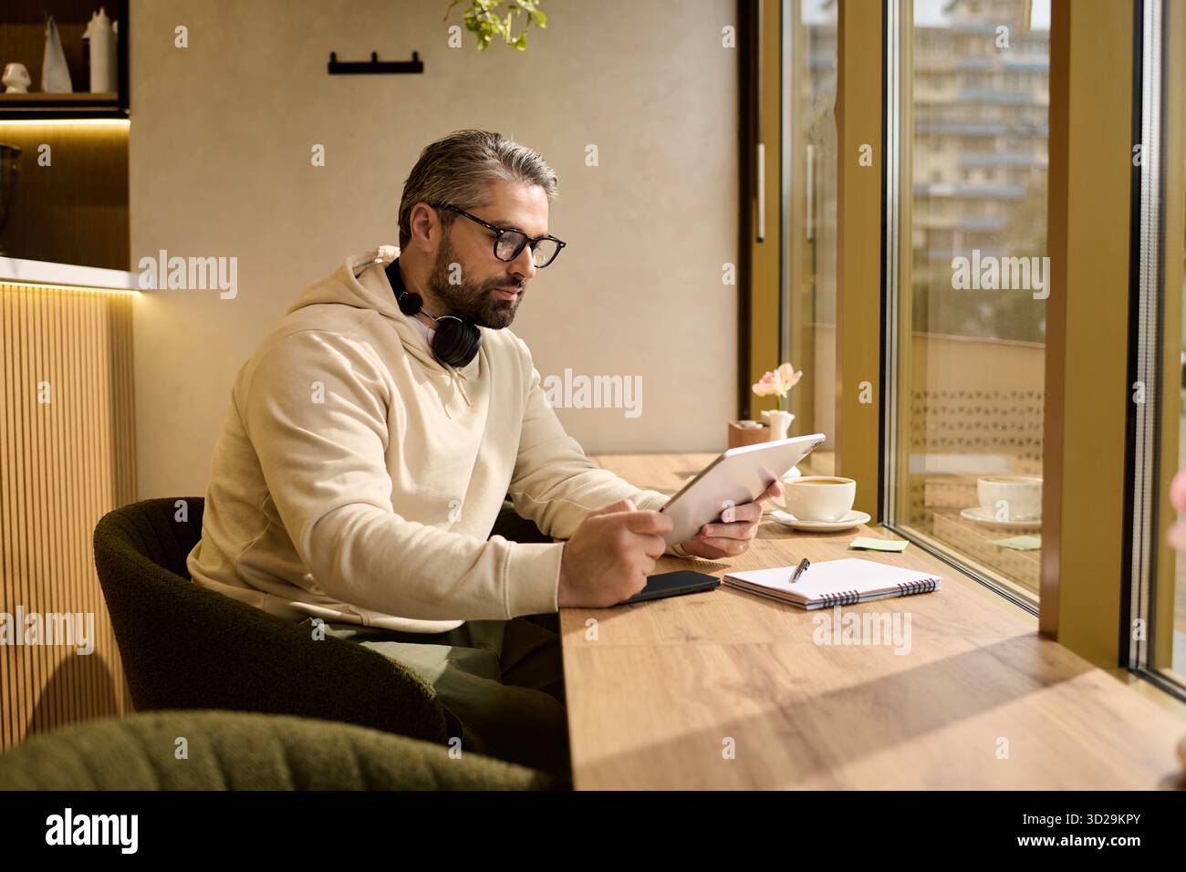 Bell'uomo maturo siede in un caffè caldo, concentrato sul suo tablet mentre sorseggia un caffè. Foto Stock