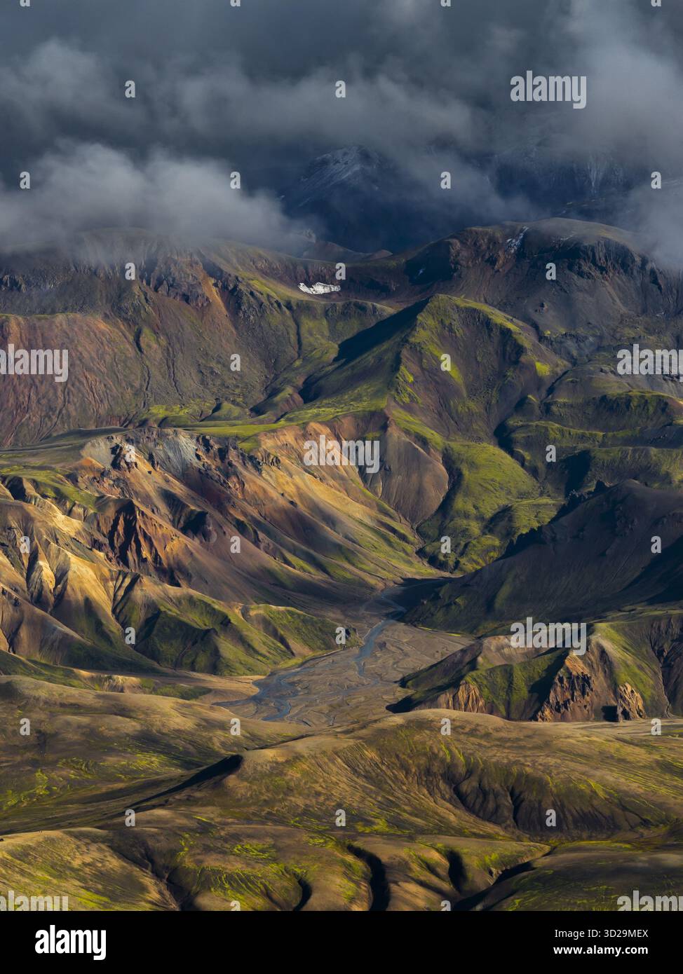 Vista aerea di terreni accidentati dipinti con sfumature di verde, oro e ruggine, sotto un baldacchino di nuvole ripide, Highlands dell'Islanda, Sveitarfélagið Horn Foto Stock