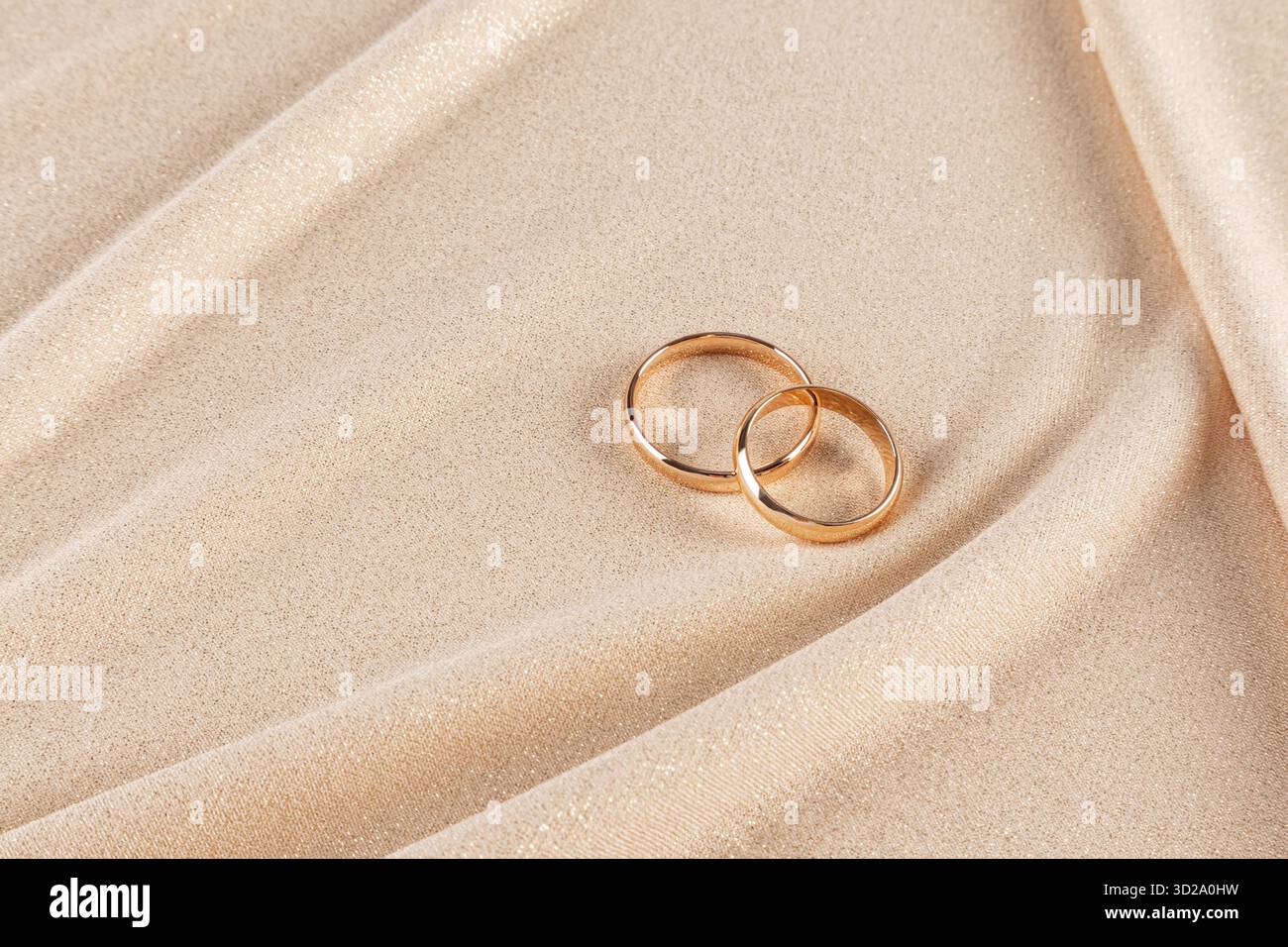 Due fedi nuziali dorate sono adagiate su un elegante sfondo in tessuto dorato con morbide onde. Uno spazio di copia. Mockup per il design di matrimoni. invito. cartolina Foto Stock