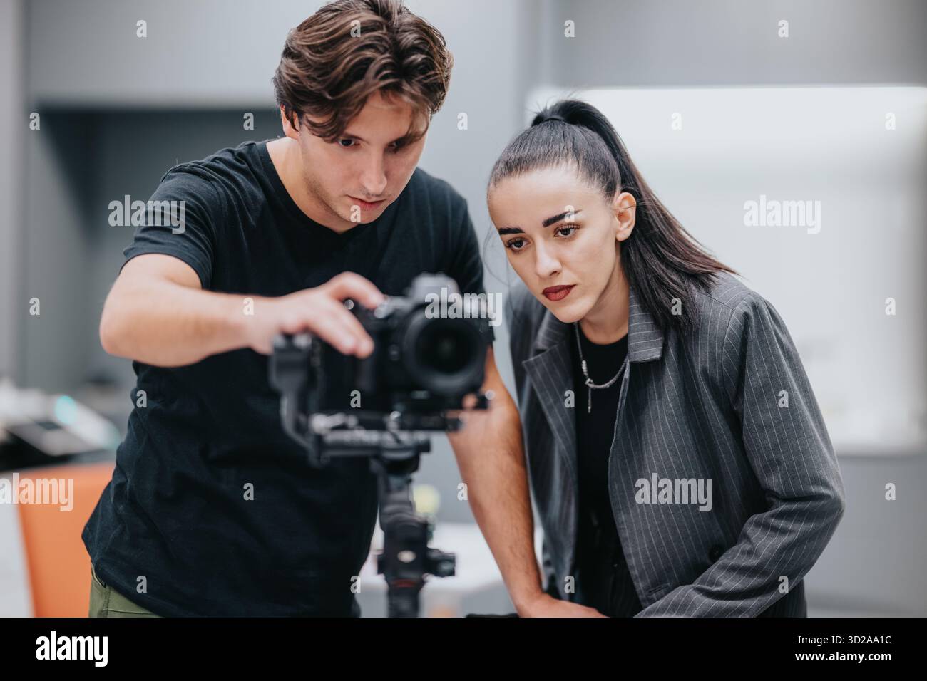Due giovani professionisti collaborano alla configurazione della fotocamera in uno studio moderno durante una sessione fotografica Foto Stock