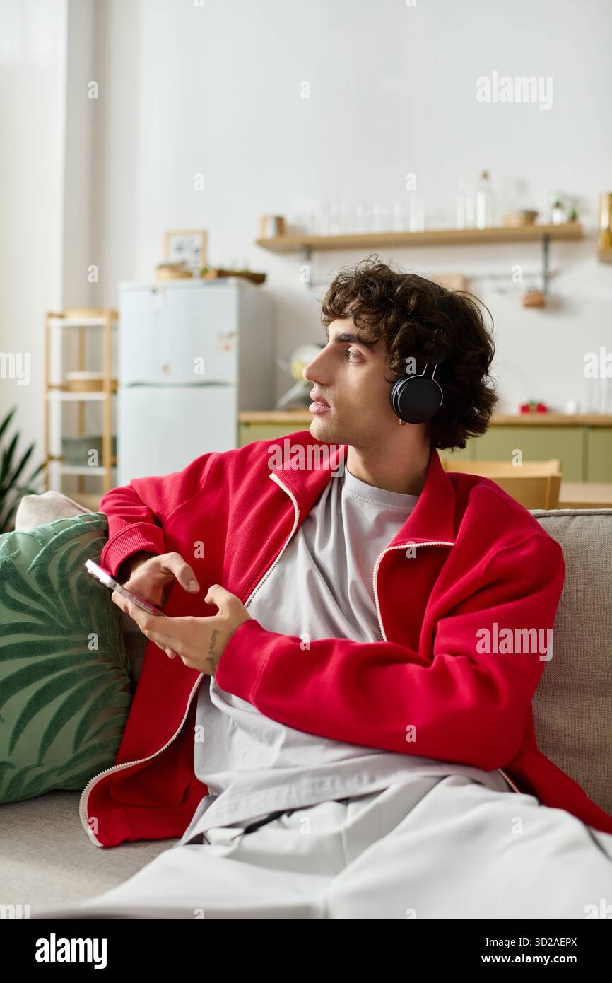 Un uomo affascinante in un abbigliamento alla moda ascolta la musica mentre ti rilassi comodamente a casa. Foto Stock