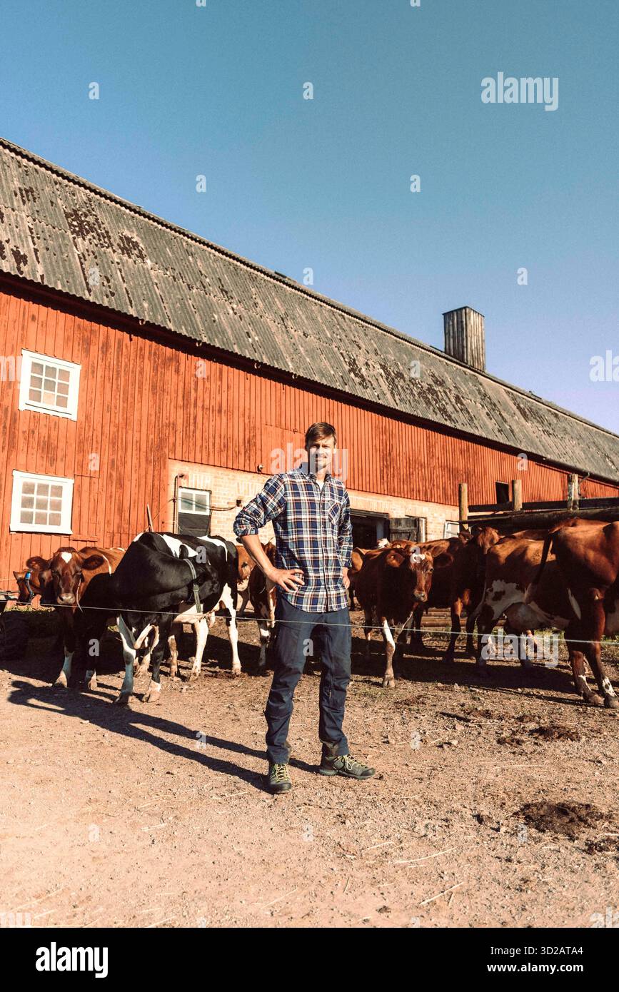 L'intera lunghezza dell'agricoltore maschile che posa con le braccia akimbo davanti al fienile Foto Stock