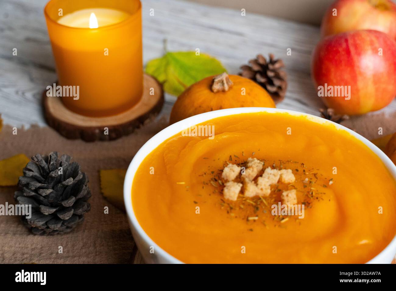 Caldo scenario autunnale con minestra di zucca cremosa, crostini, mele, zucche, pinne, e a lume di candela. Perfetto per ricette autunnali, blog gastronomici e stagionali Foto Stock