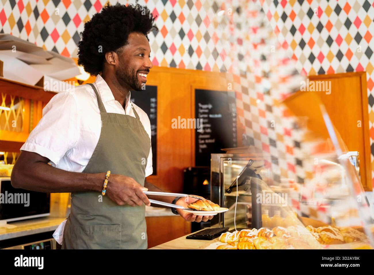 Un barista sorridente che serve croissant freschi al bar Foto Stock