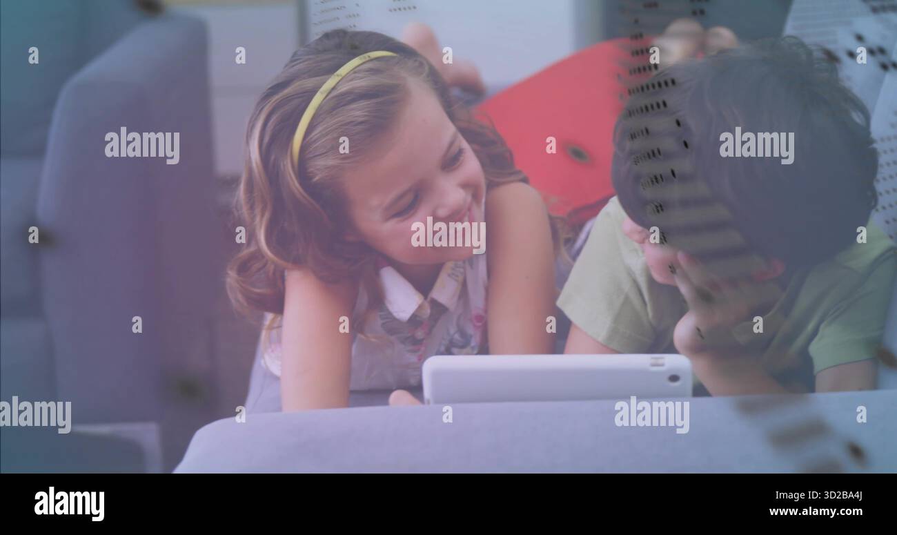 Fratello e sorella pendenti che guardano un tablet bianco sul divano in soggiorno, con cuscino rosso Foto Stock