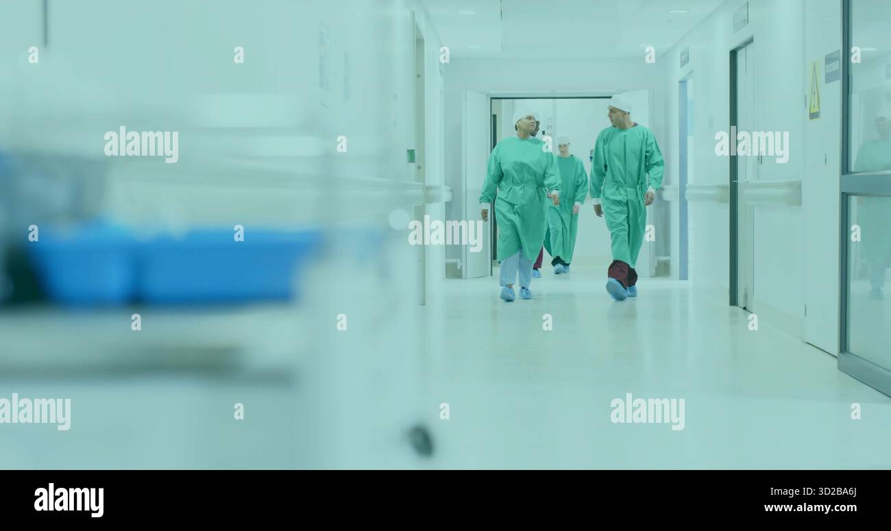 Cammina squadra chirurgica indossando scrub e copriscarpe lungo il corridoio dell'ospedale, con carrello Foto Stock