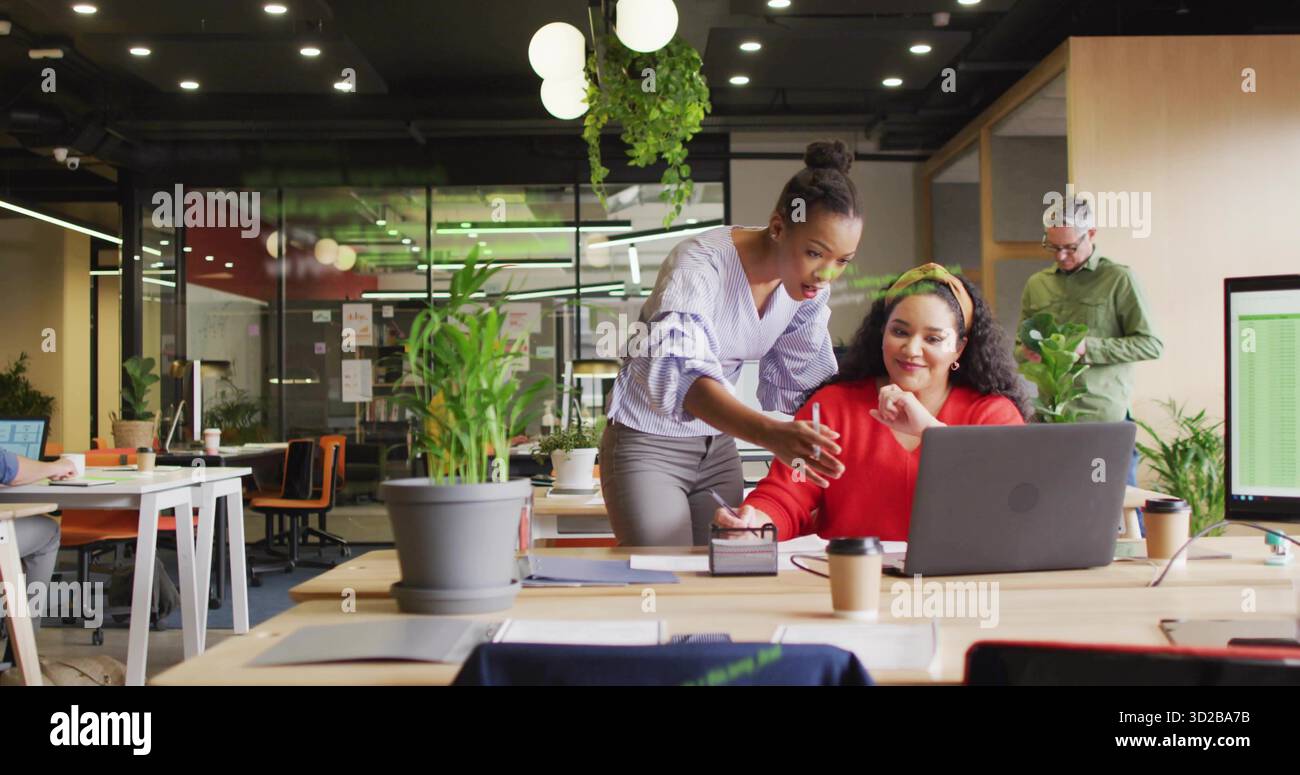 Collaborare con due colleghi donne che condividono idee in un ufficio open space, con laptop e tazze da caffè Foto Stock