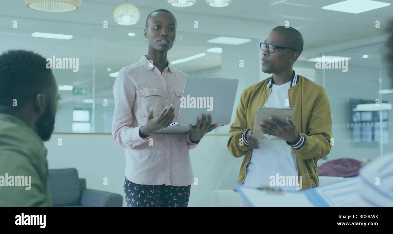 Donna che presenta un notebook al centro in una moderna sala d'ufficio, con tablet, cartella, divano grigio Foto Stock