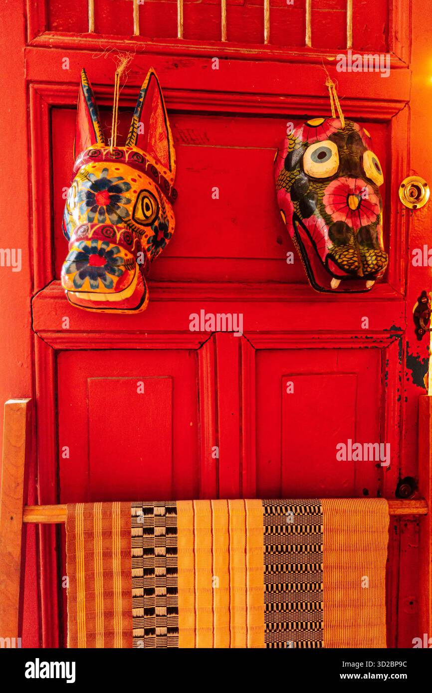 Merida, Yucatan, Messico, due maschere appese ad una porta rossa. Le maschere sono colorate e hanno un design unico. La porta è rossa e ha un telaio in legno Foto Stock
