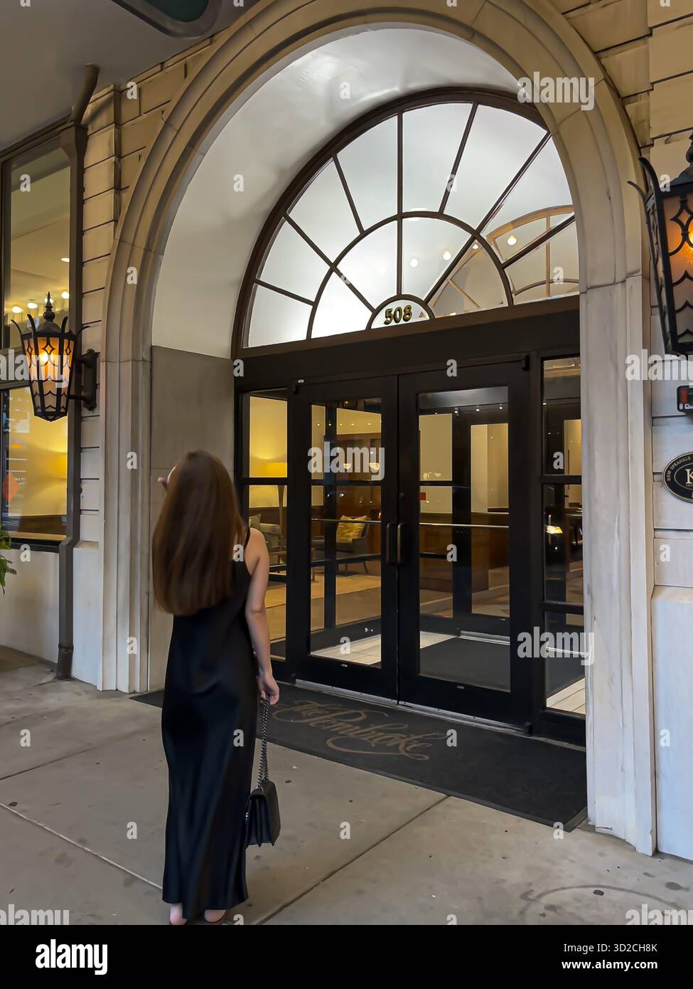 Donna che entra nell'elegante edificio con finestre ad arco in vetro, cartello 508 sopra la porta, scena serale della città, Knoxville, Tennesse - Immagine stock catturata con smartphone