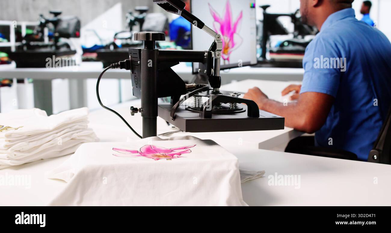 Giovane uomo che utilizza la macchina per il trasferimento di calore per stampare magliette personalizzate. Foto Stock