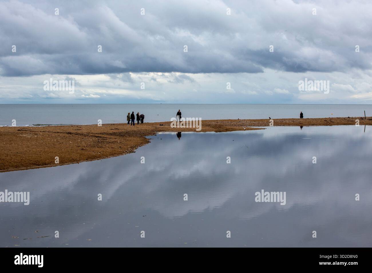 Riflessioni sull'acqua a Charmouth Dorset. Persone in riva al mare in ombra con cieli drammatici Foto Stock