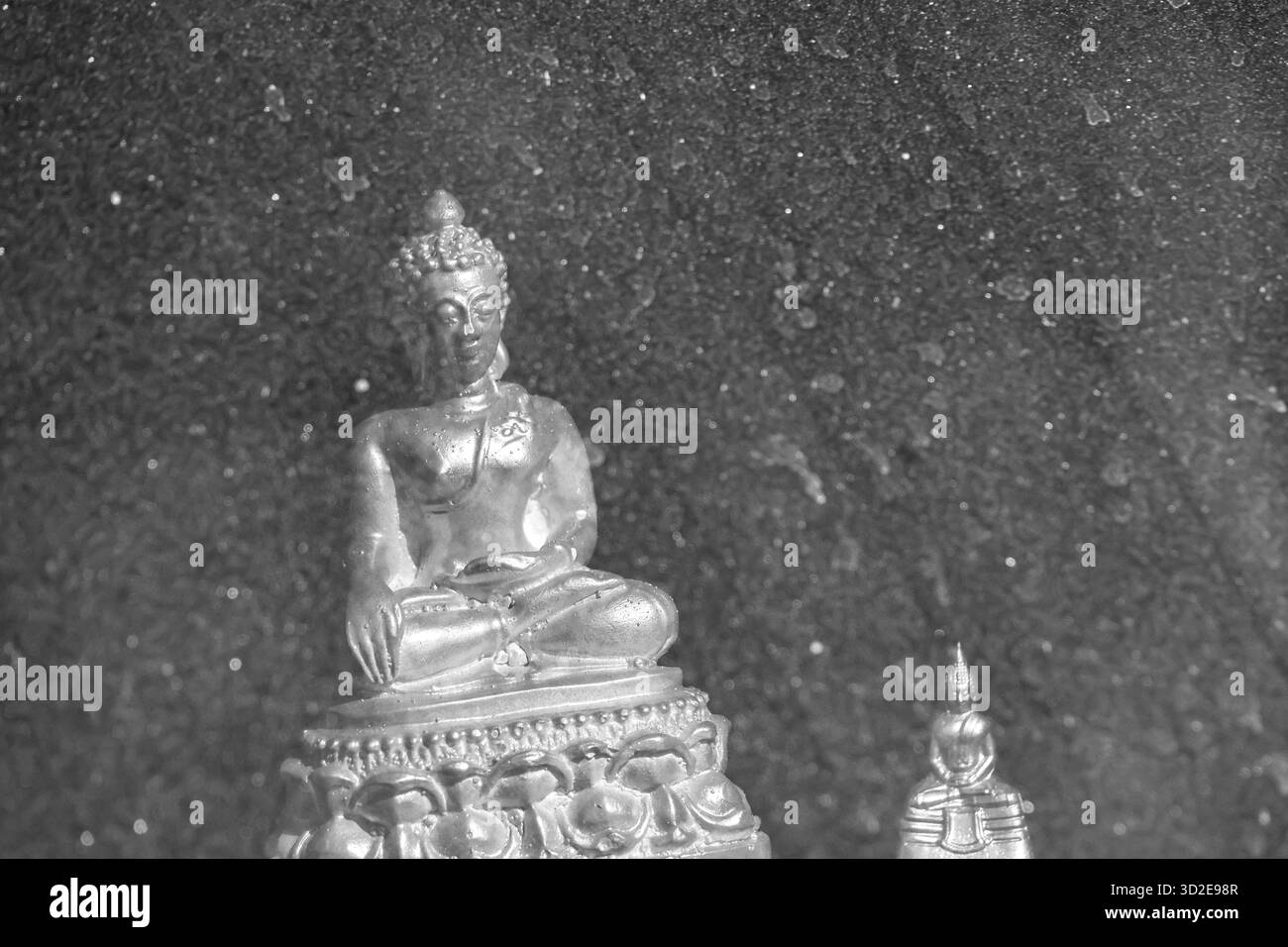 Serena fotografia in bianco e nero della statua del Buddha in meditazione. Questa icona spirituale del buddismo si trova con calma su sfondo di pietra scura e testurizzata Foto Stock