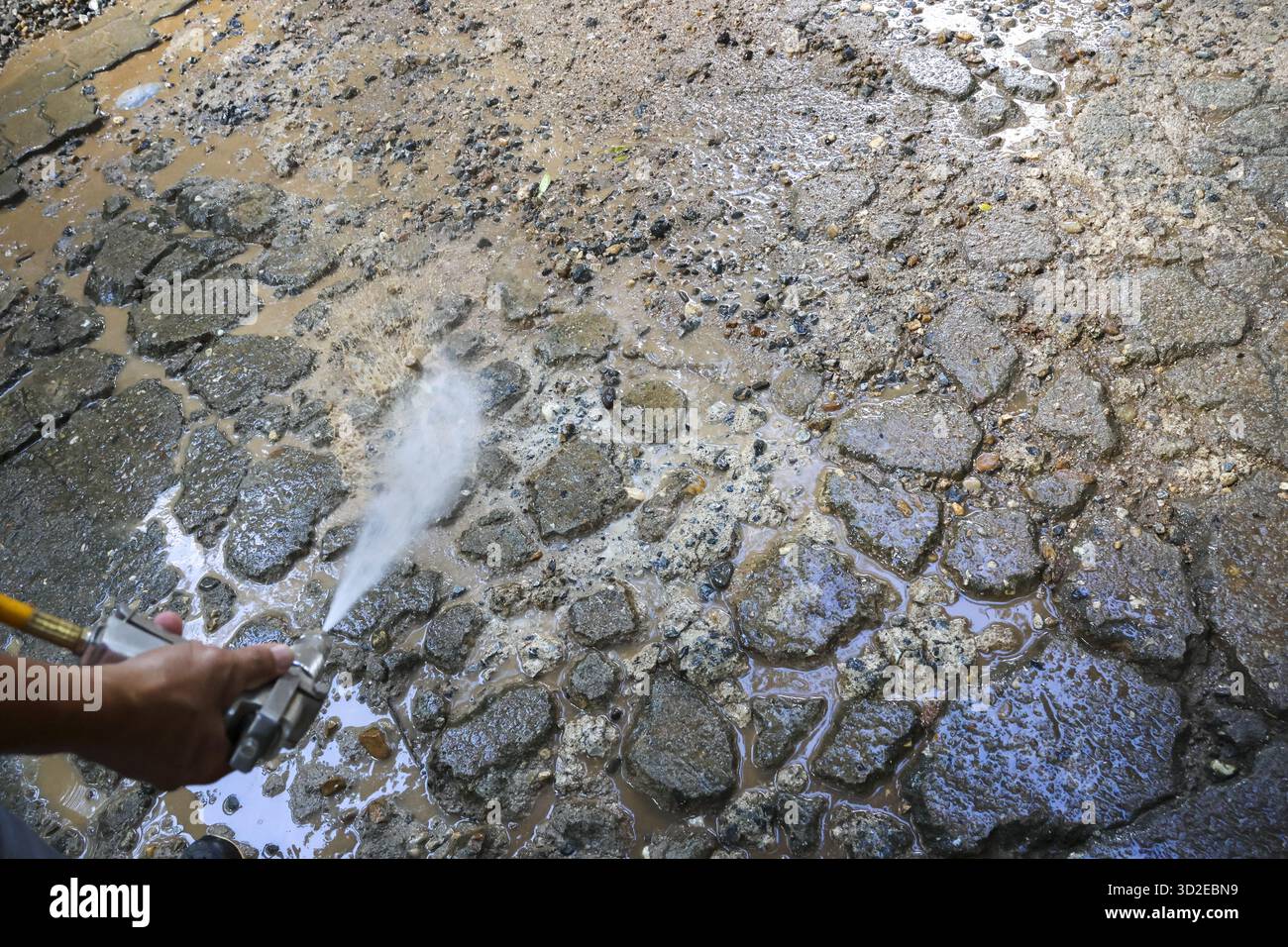 Lavoratore concentrato che pulisce pavimenti in pietra sporca con tubo flessibile dell'acqua ad alta pressione. Lavori di manutenzione edile che eliminano fango e sporcizia da un vecchio ciottolo Foto Stock