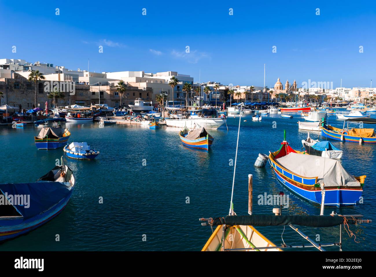 Barche luzzu colorate nel porto di Marsaxlokk con lo skyline della chiesa Foto Stock