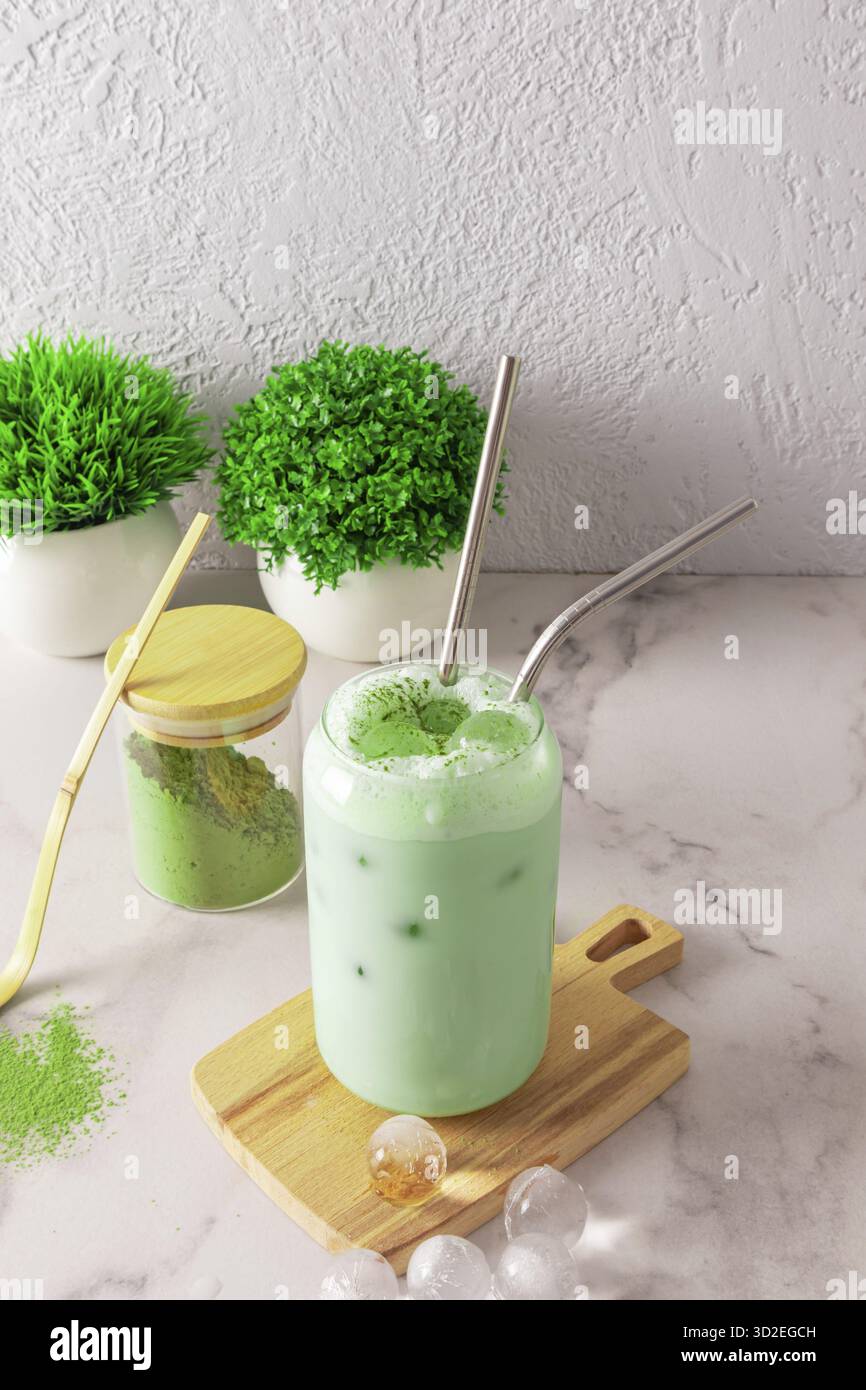 Latte di té matcha ghiacciato in un bicchiere moderno a forma di lattina di birra con paglia e ghiaccio a forma di palla si trova su un asse di legno Foto Stock