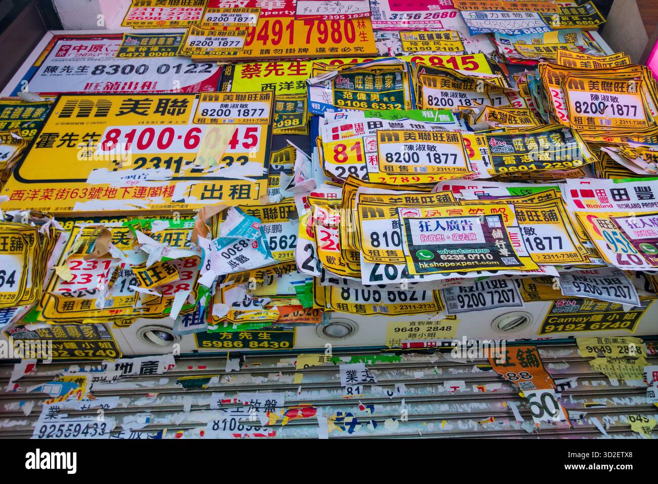 Un denso collage di annunci pubblicitari colorati per il noleggio e volantini d'affari disposti su un muro in una scena urbana di Hong Kong. Foto Stock