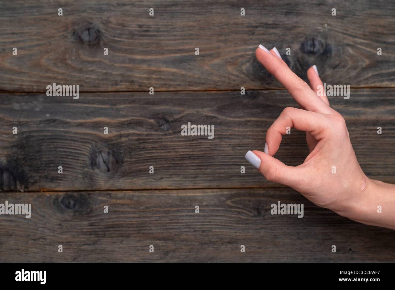 Mano della donna che forma un segno OK su sfondo di legno, creando per esprimere approvazione e accordo. gesto di positività e comunicazione di successo. FEM Foto Stock