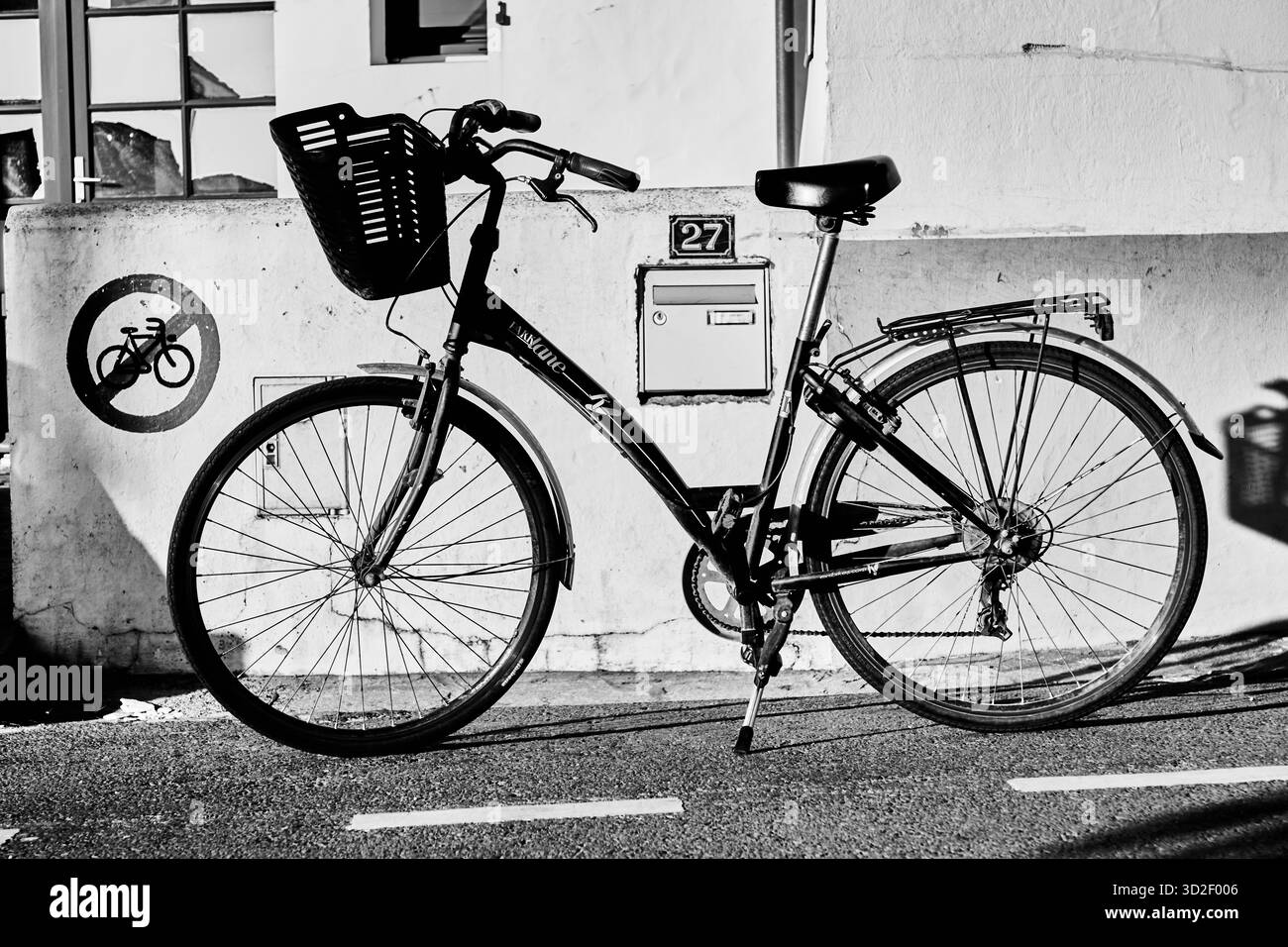 Una bicicletta nera parcheggiata di fronte a un muro bianco con un cartello "27" e un simbolo di divieto di utilizzo della bicicletta. Foto Stock