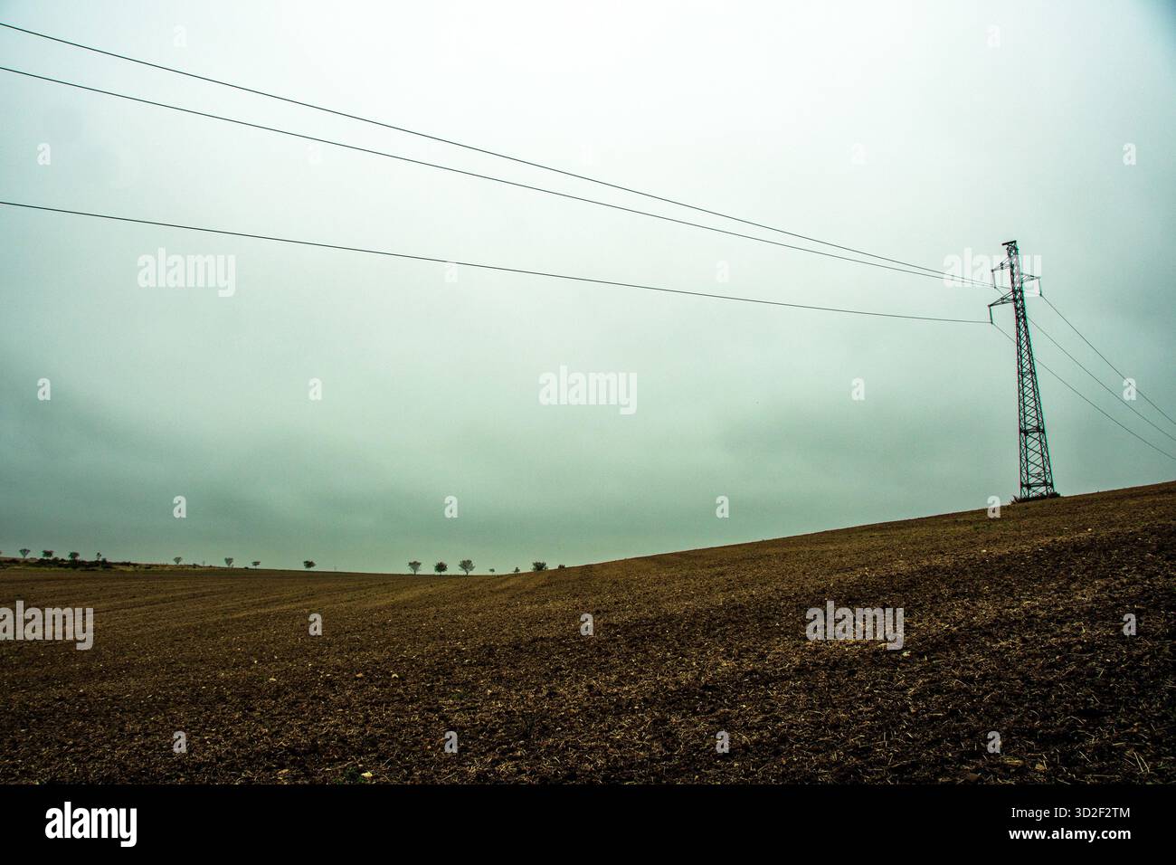 Una torre di trasmissione di potenza metallica si trova su un campo arato sotto un cielo grigio e coperto. Francia Foto Stock