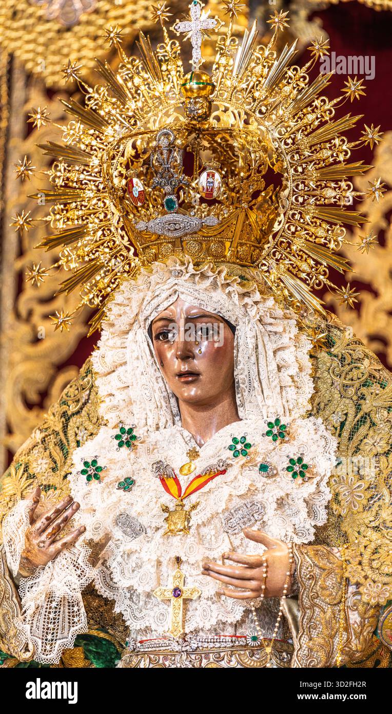 A Siviglia, la Vergine della speranza Macarena è decorata con abiti intricati e corona d'oro. La folla si riunisce per onorarla durante una solenne processione. Foto Stock