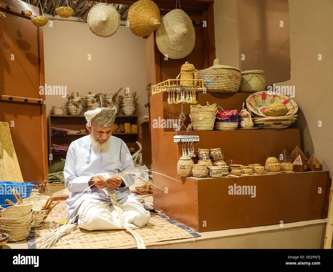 Mascate, Oman - 24 dicembre 2024: Un artigiano omanita tessera artigianato tradizionale a partire da foglie di palma essiccate, noto come "khous", al Mascate Festival, Oman. Foto Stock