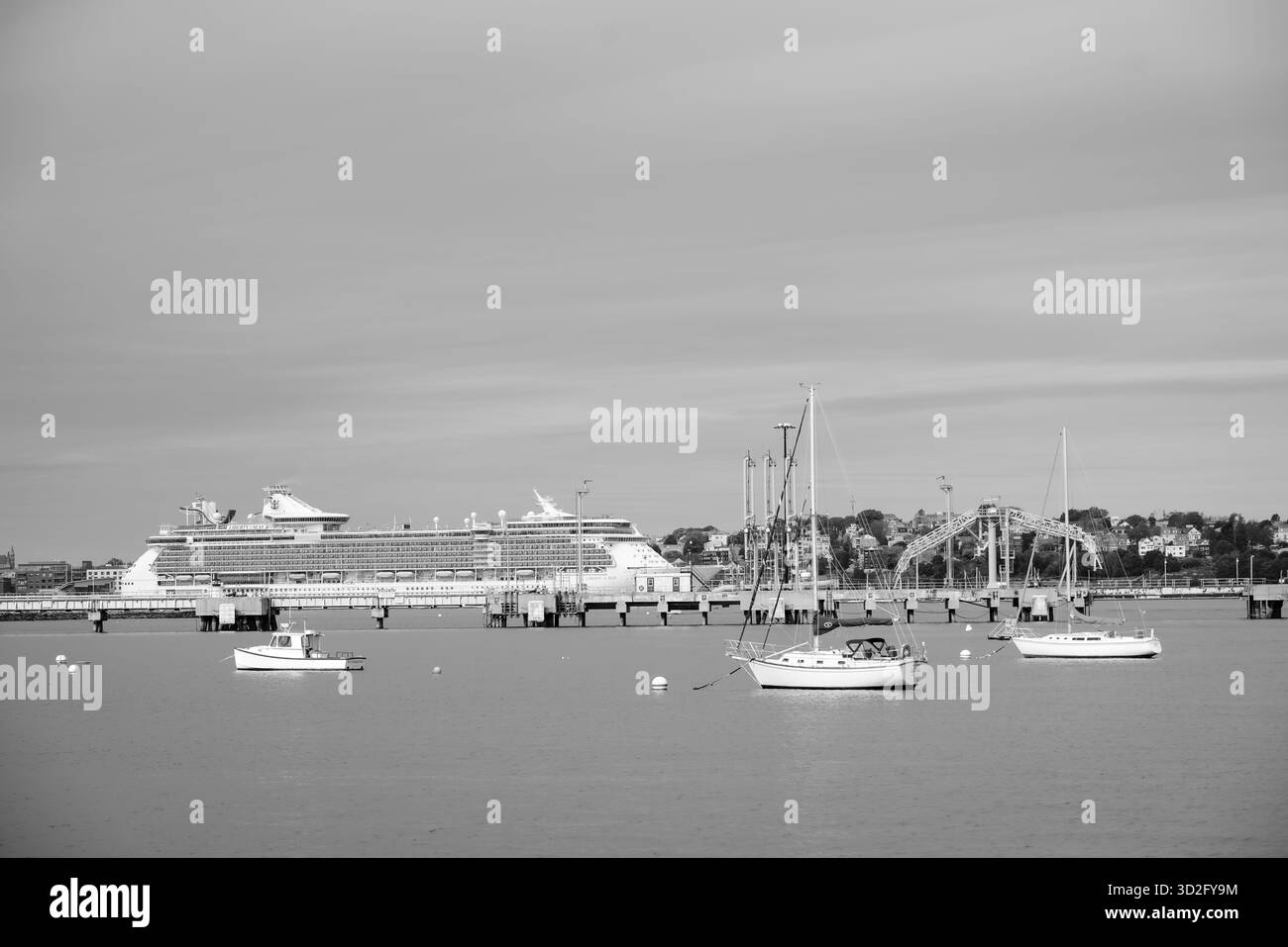 Vista in bianco e nero della Liberty of the Seas attraccata nel porto di Portland con piccole barche che galleggiano nelle vicinanze sotto un cielo calmo Foto Stock
