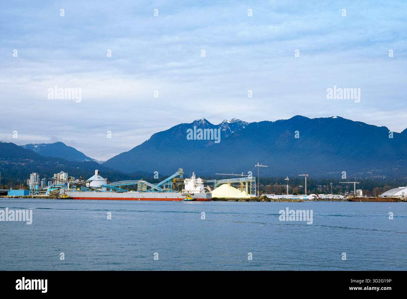 Un'ampia vista di un porto industriale adagiato su montagne innevate, con strutture di trasporto, strutture di carico e acque calme del porto Foto Stock