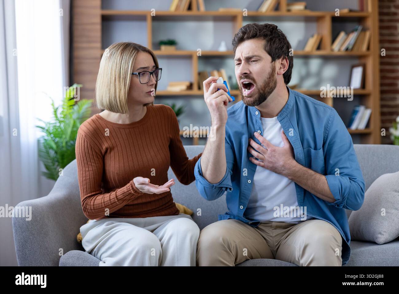 Uomo che soffre di asma attacco e lotta per il respiro, utilizzando un inalatore mentre una donna preoccupata offre supporto, evidenziando problemi di salute e difficoltà respiratorie Foto Stock