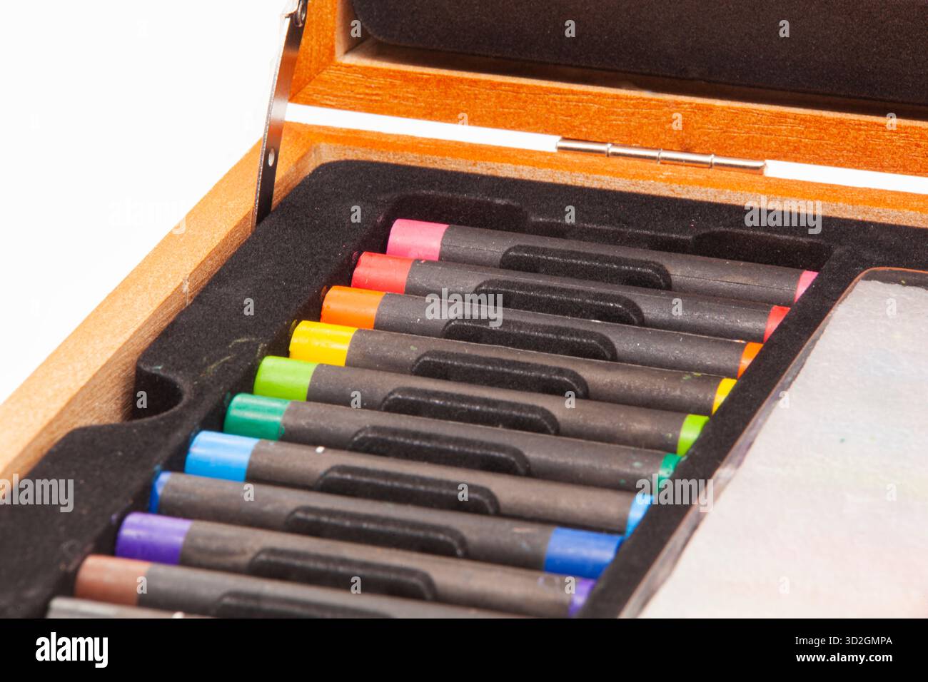 Primo piano di una serie di pastelli pastello luminosi e quadrati disposti a colori negli scomparti di un vassoio nero all'interno di una cassa di legno aperta. Foto Stock