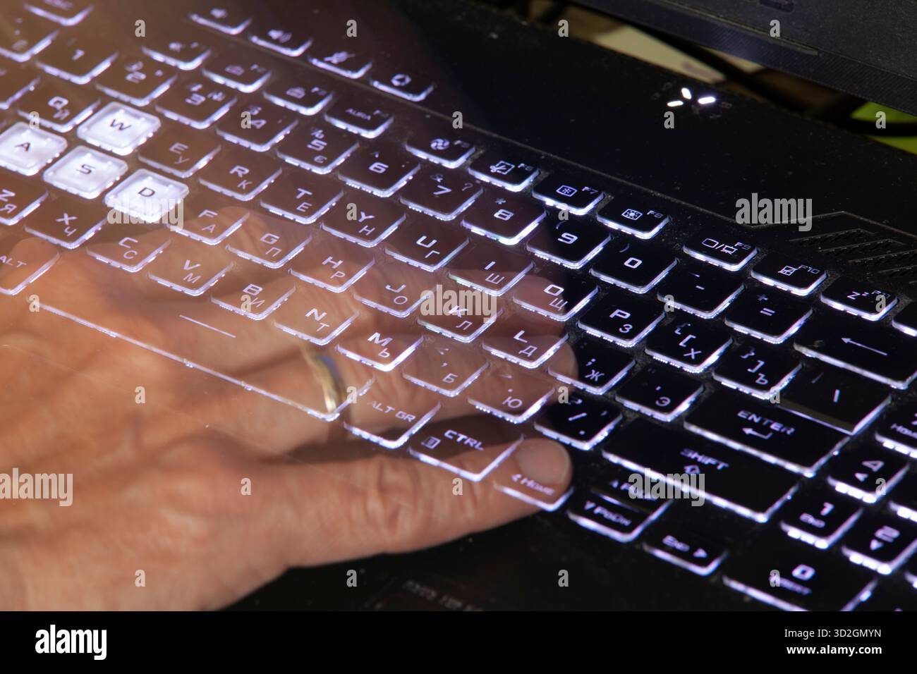 Primo piano di una mano premendo il tasto Home su una tastiera nera del notebook con retroilluminazione bianca. La tastiera contiene caratteri russi e inglesi. Foto Stock