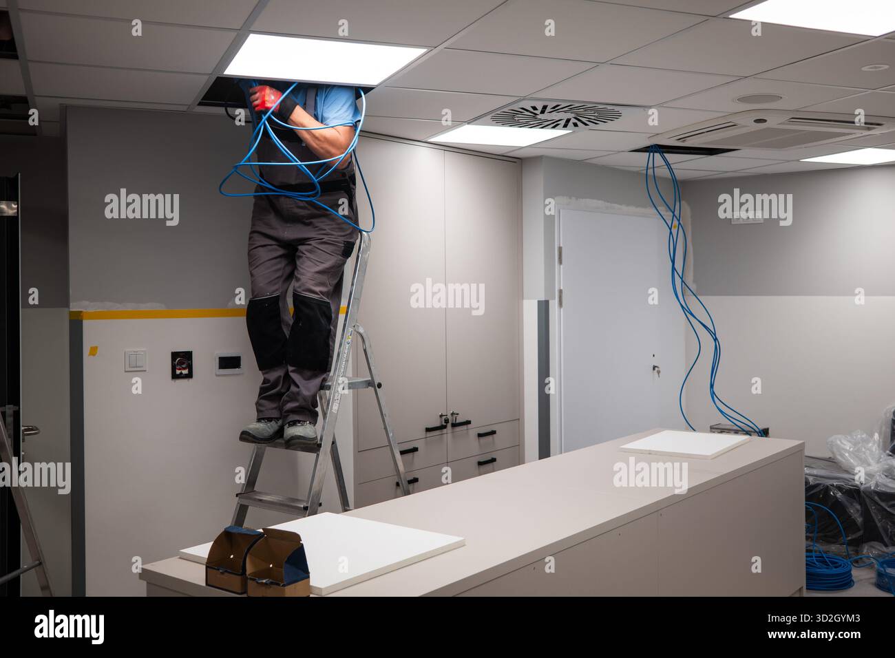 Un elettricista fa passare i cavi su un controsoffitto in una nuova stanza Foto Stock
