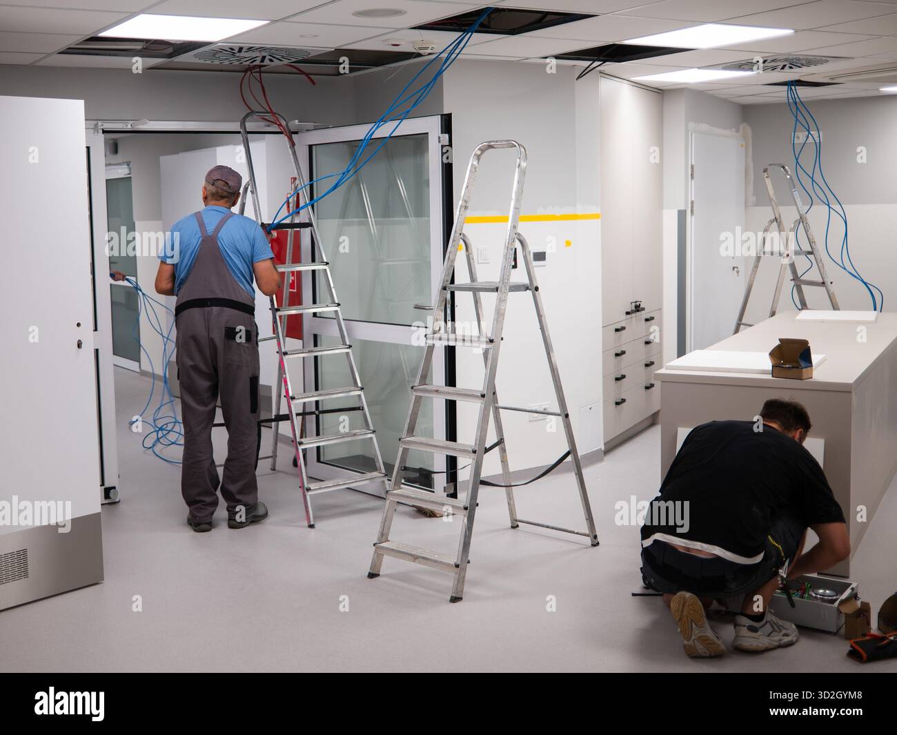 Un elettricista fa passare i cavi su un controsoffitto in una nuova stanza Foto Stock