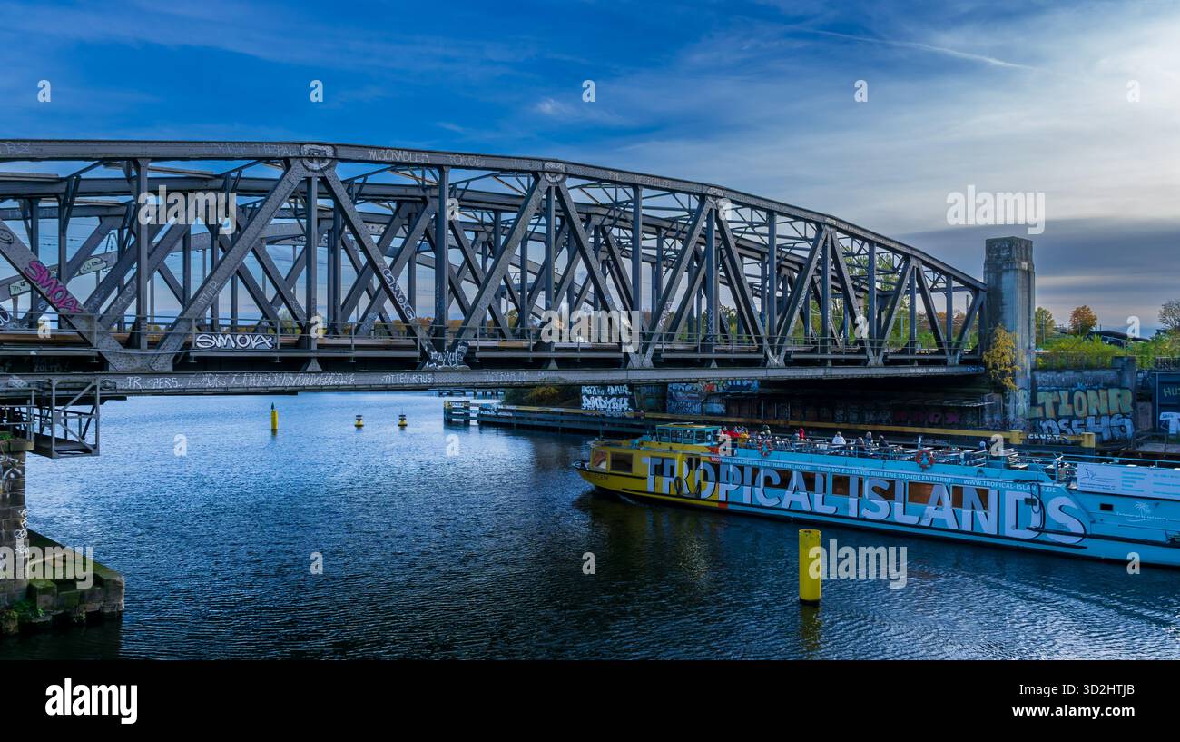Tour in barca delle “Isole tropicali” che naviga sul fiume Sprea nel quartiere Treptow di Berlino mentre passa sotto un grande ponte ferroviario storico in acciaio. Foto Stock