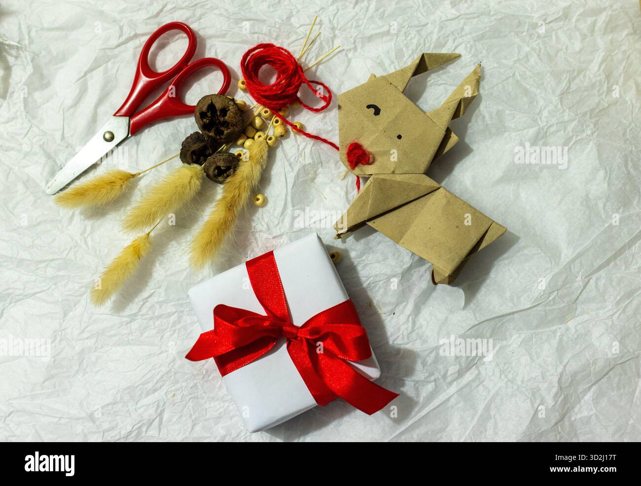 Confezione regalo fatta a mano circondata da decorazioni naturali rustiche, filati, forbici, colla e accoglienti accenti stagionali. Vista dall'alto. Concetto di riciclaggio e handma Foto Stock