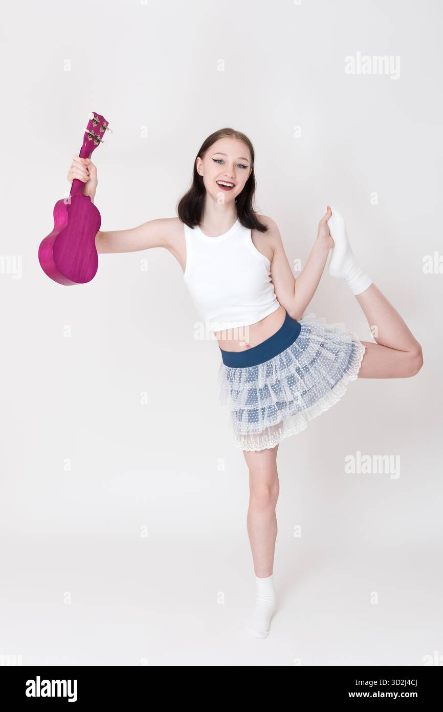 Donna giubilante esperta di ukulele e ginnastica che tiene in mano il suo strumento, esegue movimenti coreografici e proietta alla telecamera. Giovane a tutta lunghezza Foto Stock