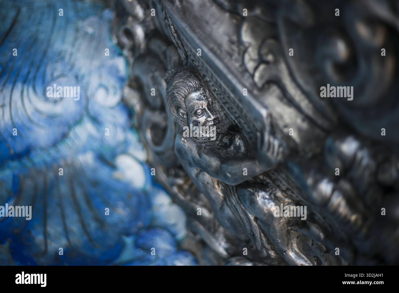 Texture metallizzata con dettagli blu. Una scultura ornata mostra motivi dettagliati e rilievi antichi e scuri, creando misteriosi e. Foto Stock