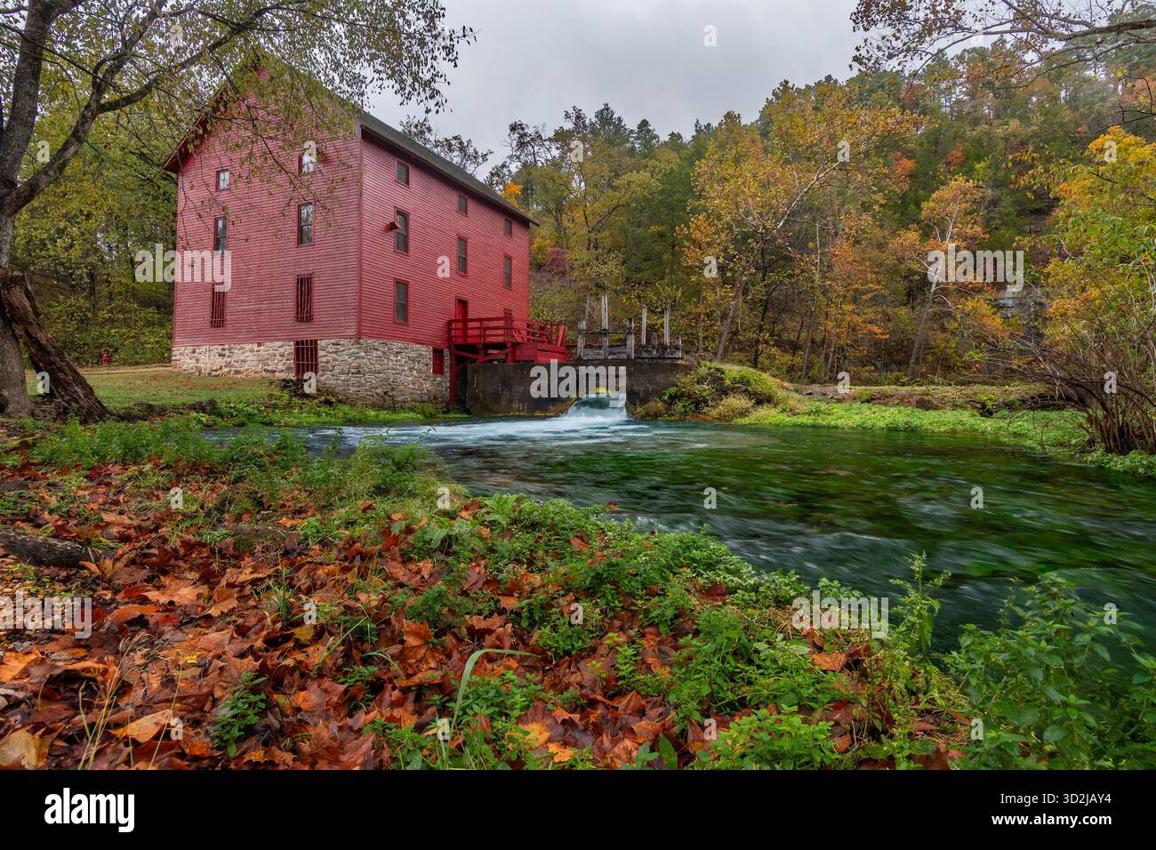 L'iconico Red Alley Spring Mill sorge accanto a una vibrante sorgente turchese, circondata dalle ricche sfumature arancioni e gialle del fogliame autunnale. Foto Stock