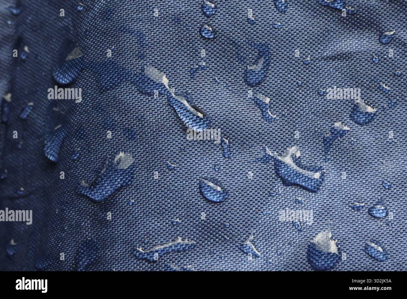 Pulizia ravvicinata del tessuto impermeabile blu con gocce di acqua dolce sulla superficie ruvida. sfondo protettivo in tessuto resistente all'acqua Foto Stock