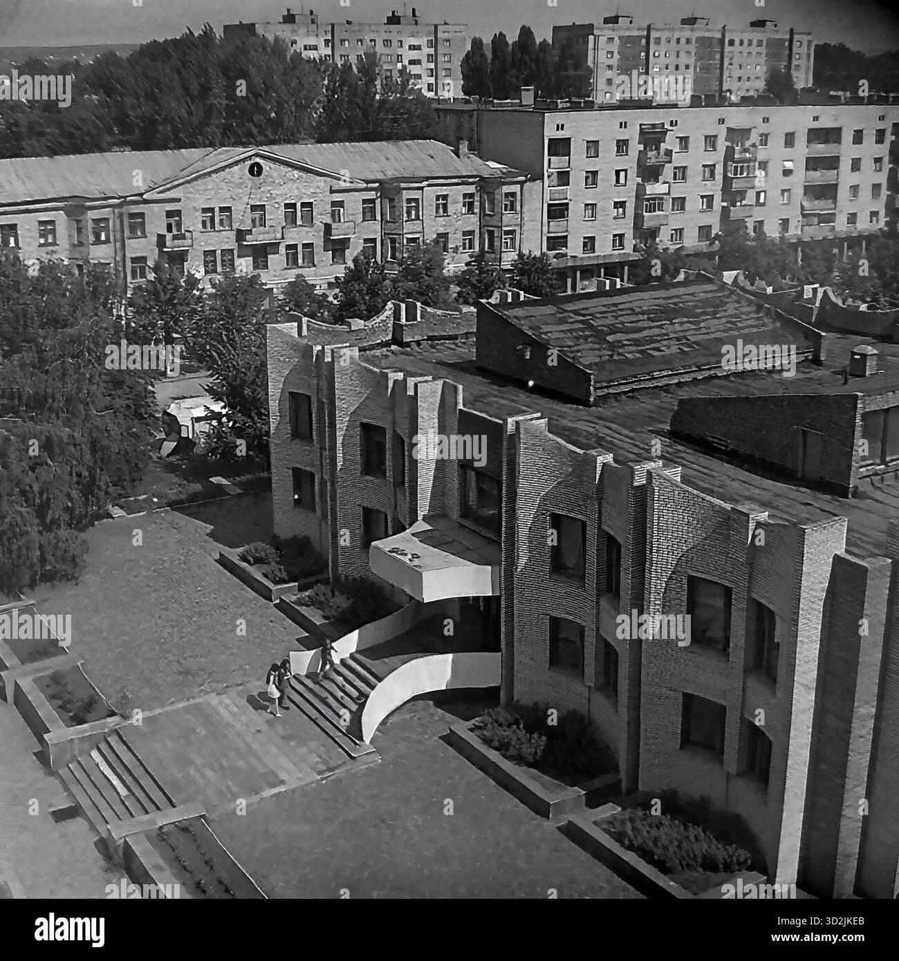 Archivio foto in bianco e nero da Sloviansk, Ucraina, luglio 1997. Questa vista ad alto angolo mostra la biblioteca centrale in Piazza della Rivoluzione d'ottobre (ora Piazza Soborna). L'edificio presenta un'architettura modernista unica in mattoni. Due donne sono sui gradini. Sullo sfondo ci sono vecchi edifici dell'epoca Stalin e nuovi blocchi di appartamenti sovietici, circondati da alberi estivi. Questo cattura il paesaggio urbano di una città post-sovietica. Foto Stock
