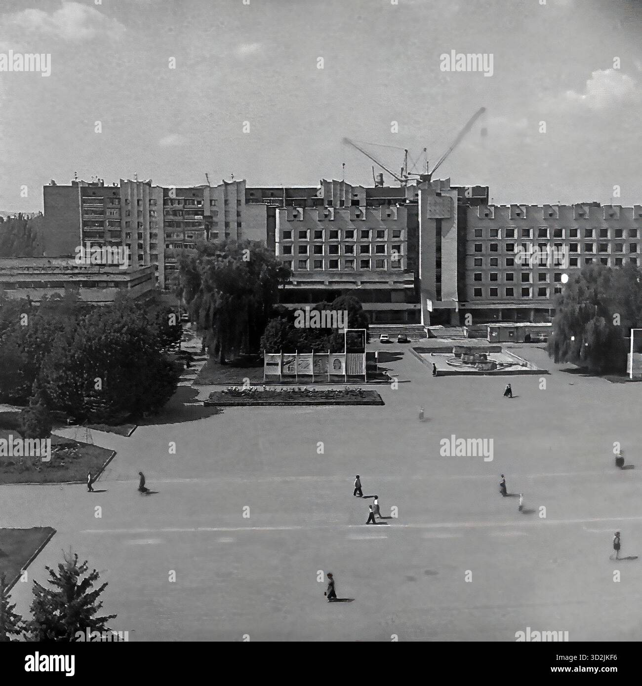 Archivio foto in bianco e nero da Sloviansk, Ucraina, luglio 1997. Questa vista ad alto angolo mostra la piazza centrale della città, Piazza della Rivoluzione d'ottobre (ora Piazza Soborna). La grande piazza aperta ha diversi pedoni che camminano attraverso di essa. Sullo sfondo si trova il massiccio edificio modernista sovietico del Consiglio comunale (Gorsovet). Grandi gru da cantiere sono visibili all'orizzonte dietro l'edificio. Questa immagine cattura il centro amministrativo della città post-sovietica. Foto Stock
