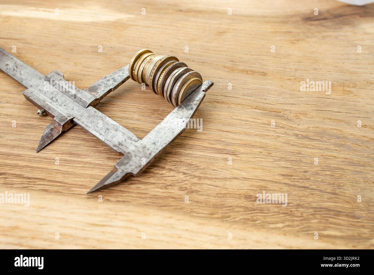 Pinza in metallo per afferrare un'alta pila di monete dorate su una scrivania in legno Foto Stock