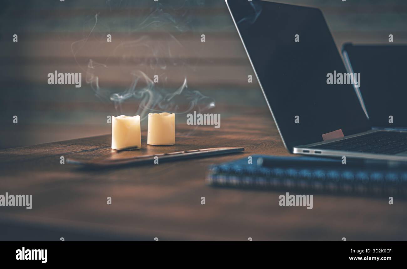 Atmosfera accogliente da ufficio a casa. Computer desktop su una scrivania di legno con notebook, penna, bastoncino aromatico e lampade a candela per una calda calma serale Foto Stock
