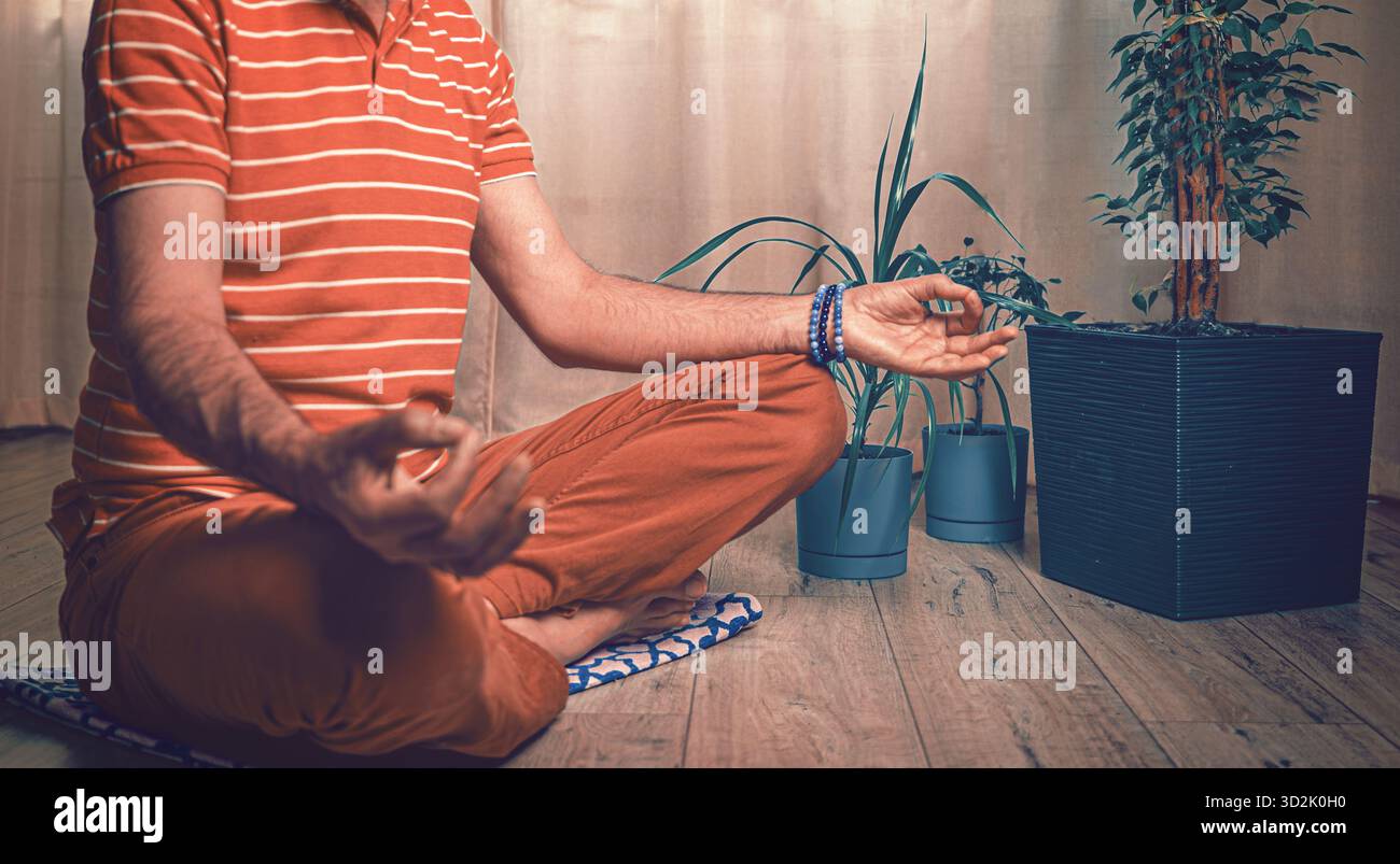 Scena pacifica di un giovane che meditava a gambe incrociate in un interno minimalista, incarnando tranquillità, equilibrio e consapevolezza di sé Foto Stock