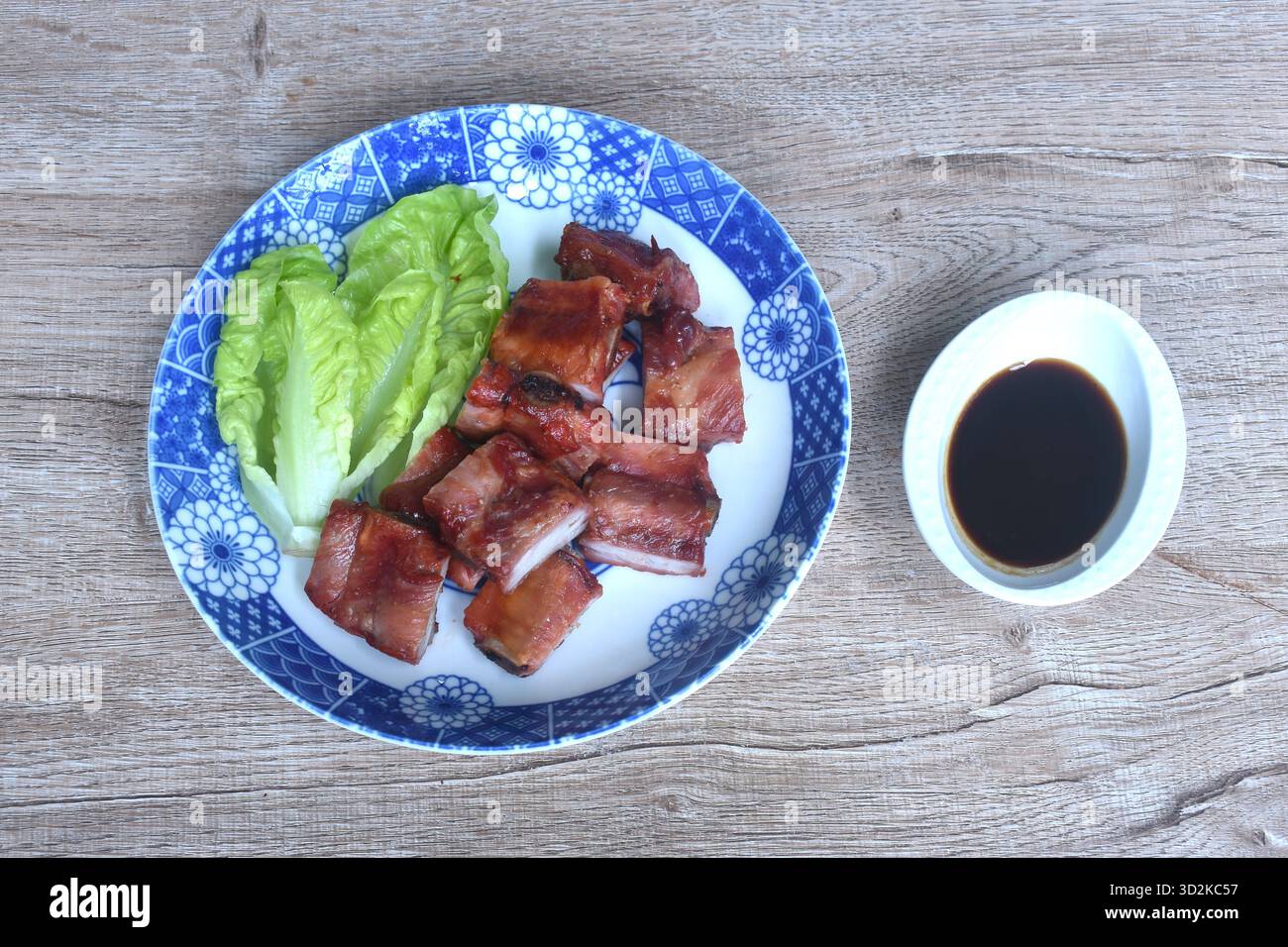 osso di maiale croccante fritto o costoletta con lattuga baby cos sul piatto e tazza con salsa dolce nera Foto Stock