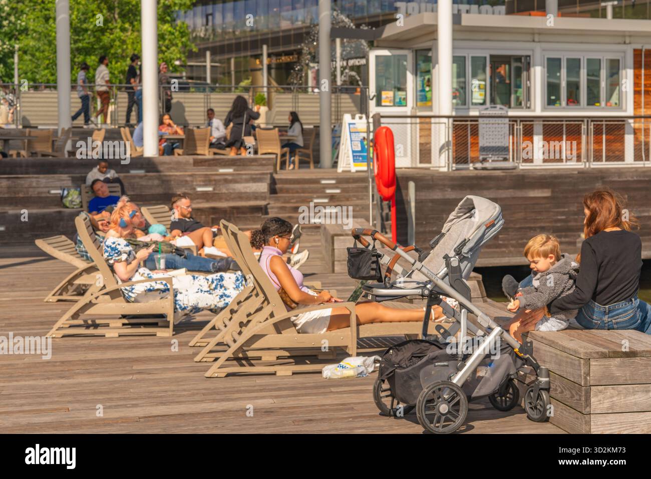 Washington D.C. USA, 24 maggio 2025. Le persone si rilassano sulle sedie e sulle panchine del lungomare di Wharf in un pomeriggio di sole. Foto Stock