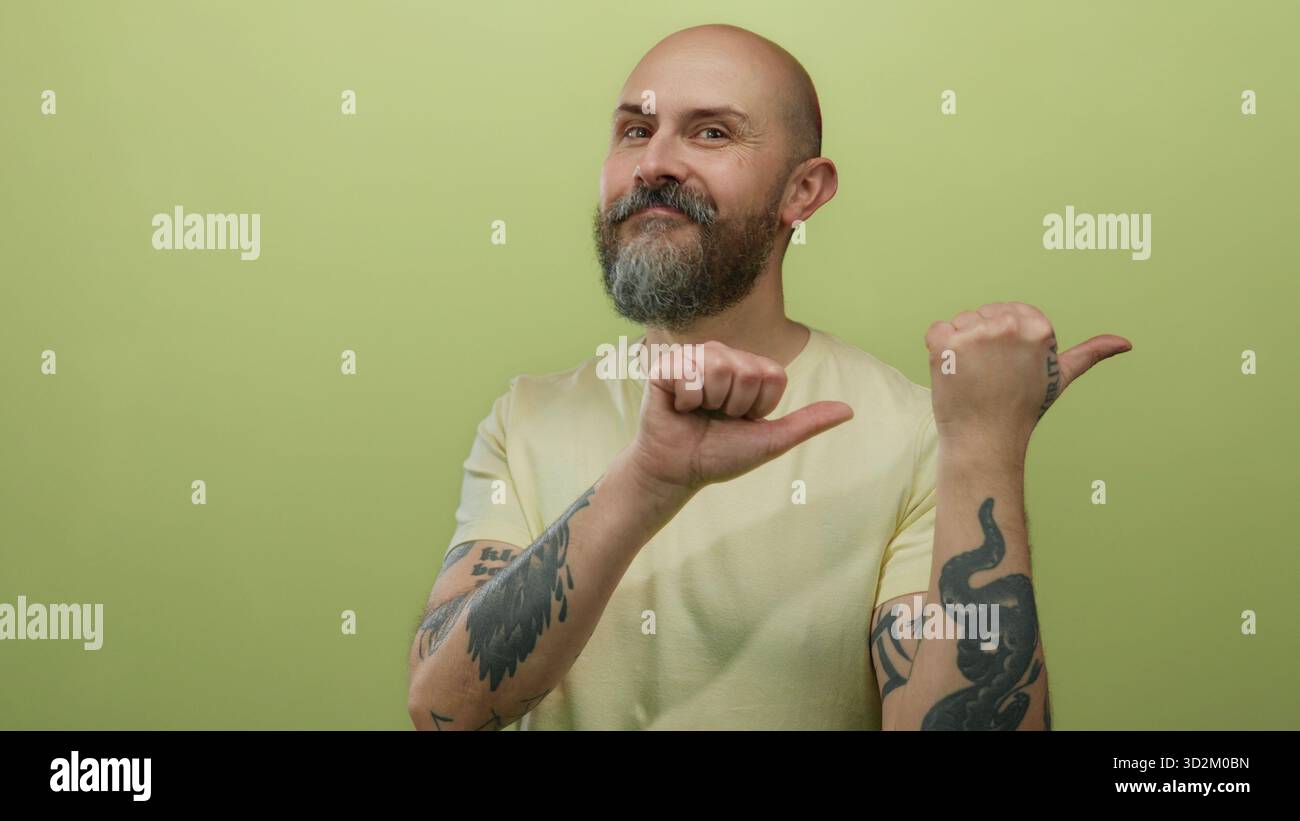 Uomo dalla barba calva con gesti tatuati con il pollice su sfondo isolato dalla parete gialla Foto Stock