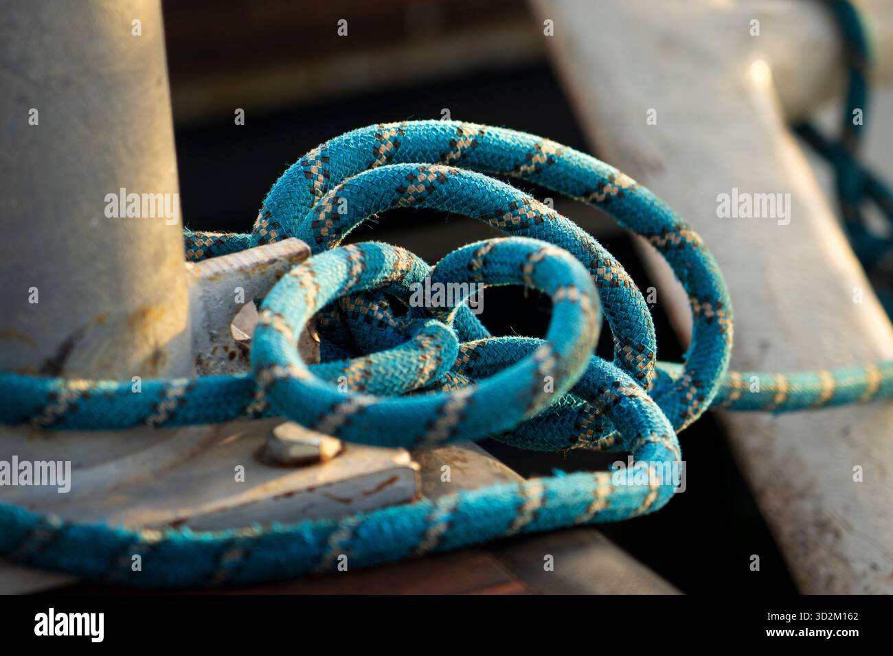 Corda blu fissata saldamente avvolta intorno al paletto di metallo su banchina di legno, nodo nautico che tiene la barca in posizione al porticciolo Foto Stock