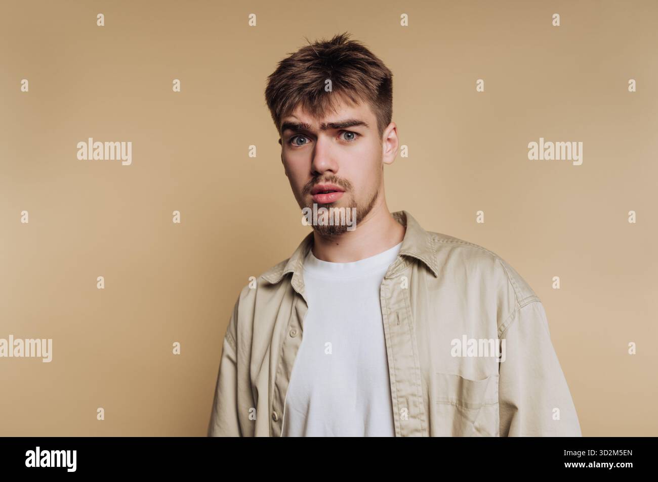 Giovane con un'espressione sorpreso in un contesto beige. Foto Stock